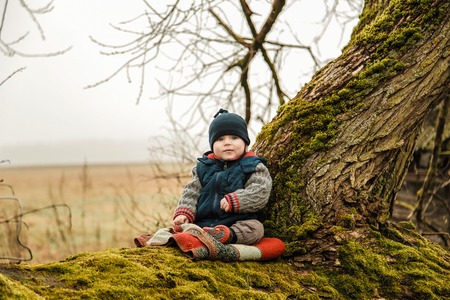 A small child sits on an old tree overgrown with mossの写真素材