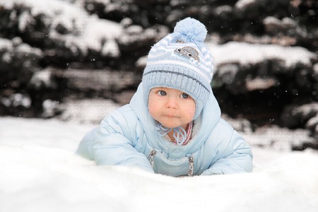A small child in a blue overalls lying on the snow near the Christmas treesの写真素材