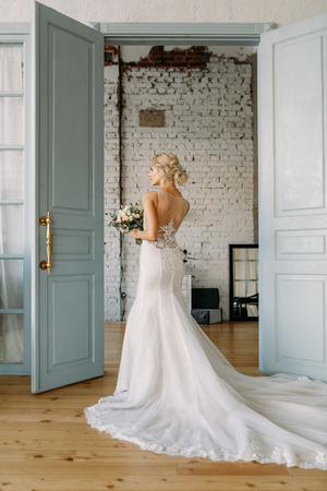 The bride in a beautiful wedding dress and a bouquet of flowers stands at the open doorの写真素材