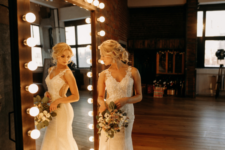 The bride in a white dress stands near the mirror and prepare for the ceremonyの写真素材