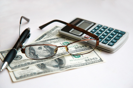 Glasses in a frame lie on dollars together with the calculator on a white tableの写真素材
