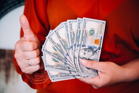 A girl in a red blouse holding American dollars and a thumb upの写真素材