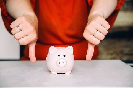 Girl shows thumb down all bad next to pink piggy Bank