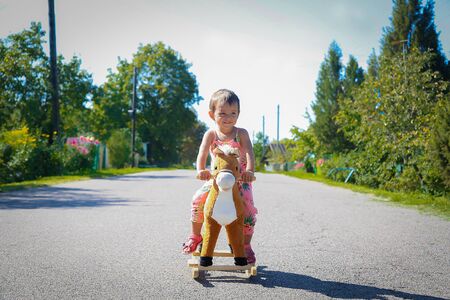 Girl swinging on toy wooden horse outdoors on roadの写真素材