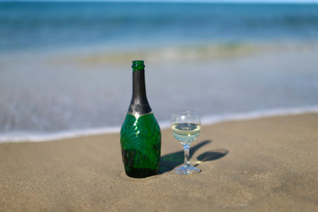 A green bottle of wine with a glass stands on the sandの写真素材