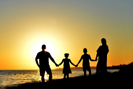 A Beautiful Family Silhouette at Sunset by the Sparkling Oceanの写真素材