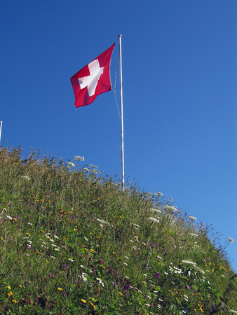 swiss flag on flagstaff at mountain peakの写真素材