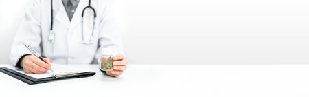 Doctor writing a prescription. He is holding a bottle of medical CBD cannabis in his hand. Legal healing cannabis for alternative medicine.の写真素材