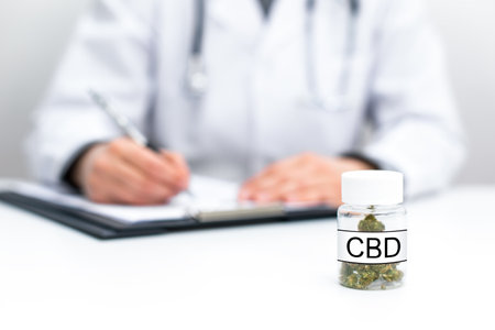 Doctor writing a prescription blank. A bottle of medical CBD cannabis on table. Close up of herbal medicinal green grass marijuana.の写真素材