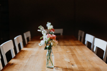 Bouquet of pink white roses stands on a beautiful wooden table in a glass vase with a dark backgroundの写真素材