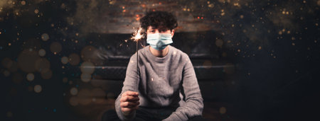 A Person is celebrating with sparkler siklvester and new year while lockdown at home. Wearing a face mask for prevention. banner. concept social distancing and lockdown during covid-19 or corona virusの写真素材