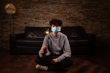 One person at new year new year's eve party. Celebrating with sparkler silvester and new year while lockdown at home. Wearing a face mask against corona. concept social distancing and lockdown.の写真素材