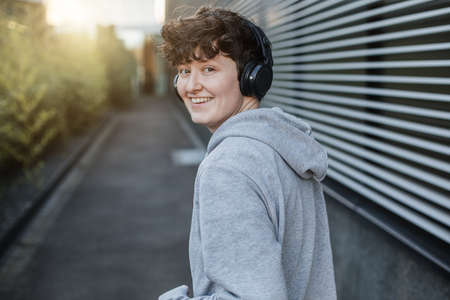 Happy person in gray sweater is jogging on the street and looks happy. Portrait of a young jogger in an urban space.の写真素材