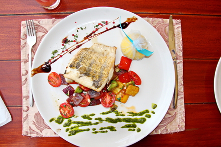 A piece of fried fish mackerel with vegetables and sauce lying on a white plateの写真素材