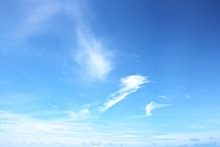 White clouds of various shapes against the blue sky and the sun above the surface of the ocean.の写真素材