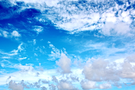 White clouds of various shapes against the blue sky and the sun above the surface of the ocean.の写真素材