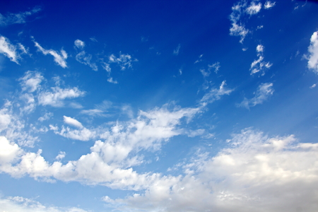 White clouds of various shapes against the blue sky and the sun above the surface of the ocean.の写真素材