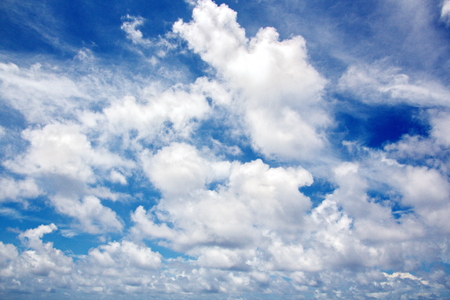 White clouds of various shapes against the blue sky and the sun above the surface of the ocean.の写真素材