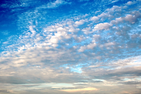White clouds of various shapes against the blue sky and the sun above the surface of the ocean.の写真素材