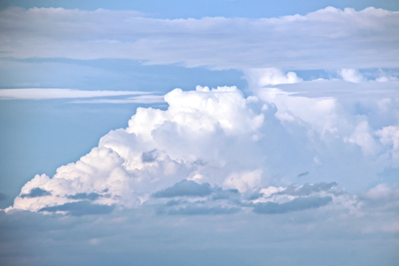 White clouds of various shapes against the blue sky and the sun above the surface of the ocean.の写真素材