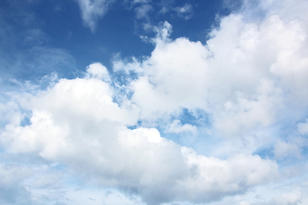 White clouds of various shapes against the blue sky and the sun above the surface of the ocean.の写真素材