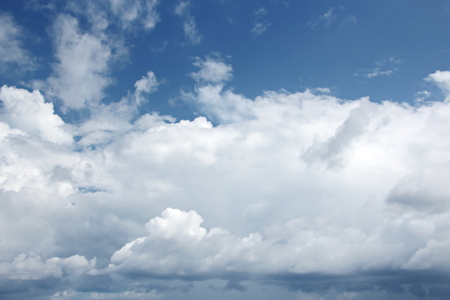 White clouds of various shapes against the blue sky and the sun above the surface of the ocean.の写真素材