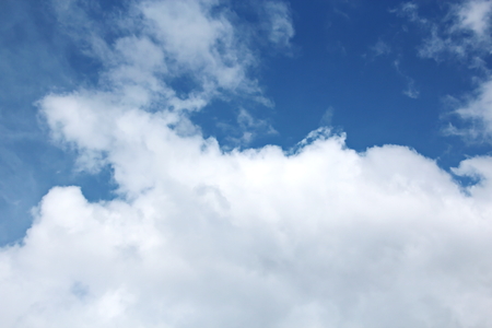 White clouds of various shapes against the blue sky and the sun above the surface of the ocean.の写真素材