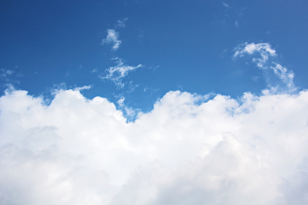 White clouds of various shapes against the blue sky and the sun above the surface of the ocean.の写真素材