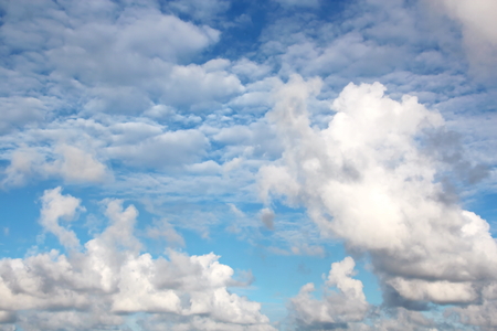 White clouds of various shapes against the blue sky and the sun above the surface of the ocean.の写真素材