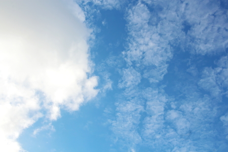 White clouds of various shapes against the blue sky and the sun above the surface of the ocean.の写真素材
