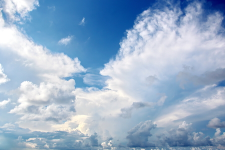White clouds of various shapes against the blue sky and the sun above the surface of the ocean.の写真素材