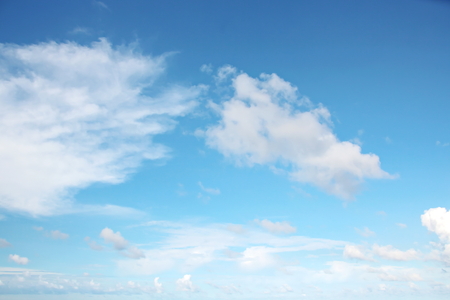White clouds of various shapes against the blue sky and the sun above the surface of the ocean.の写真素材