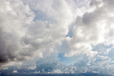 White clouds of various shapes against the blue sky and the sun above the surface of the ocean.の写真素材