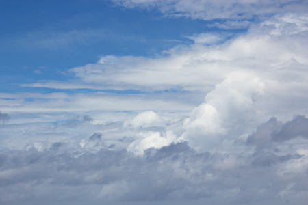 White clouds of various shapes against the blue sky and the sun above the surface of the ocean.の写真素材
