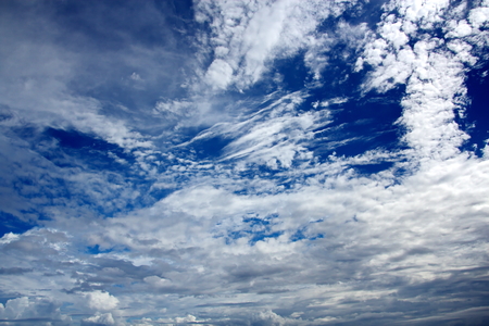 White clouds of various shapes against the blue sky and the sun above the surface of the ocean.の写真素材