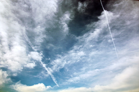 White clouds of various shapes against the blue sky and the sun above the surface of the ocean.の写真素材