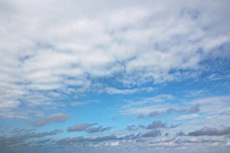White clouds of various shapes against the blue sky and the sun above the surface of the ocean.の写真素材