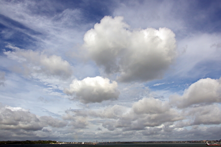 The clouds are multicolored, thunderous bizarre shapes against the blue sky and the sun above the ocean surface. The game of light and shadows in various variations of sunlight illumination of clouds and sky.の写真素材