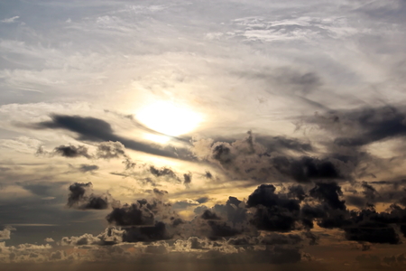 The clouds are multicolored, thunderous bizarre shapes against the blue sky and the sun above the ocean surface. The game of light and shadows in various variations of sunlight illumination of clouds and sky.の写真素材