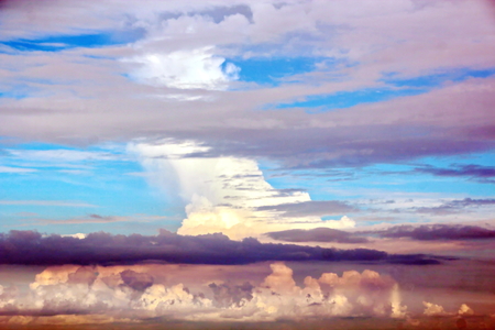 The clouds are multicolored, thunderous bizarre shapes against the blue sky and the sun above the ocean surface. The game of light and shadows in various variations of sunlight illumination of clouds and sky.の写真素材