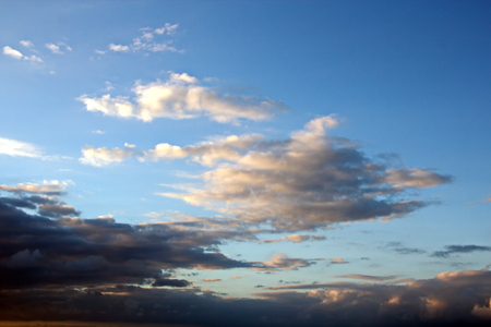 The clouds are multicolored, thunderous bizarre shapes against the blue sky and the sun above the ocean surface. The game of light and shadows in various variations of sunlight illumination of clouds and sky.の写真素材