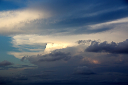 The clouds are multicolored, thunderous bizarre shapes against the blue sky and the sun above the ocean surface. The game of light and shadows in various variations of sunlight illumination of clouds and sky.の写真素材