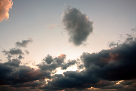 The clouds are multicolored, thunderous bizarre shapes against the blue sky and the sun above the ocean surface. The game of light and shadows in various variations of sunlight illumination of clouds and sky.の写真素材