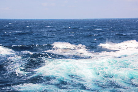 Storm waves in the world ocean. Kind of waves, crests, splashes, foam against the background of the sea horizon and the blue sky and clouds. A view of storm waves from the ship's side.の写真素材