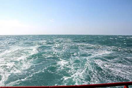 Storm waves in the world ocean. Kind of waves, crests, splashes, foam against the background of the sea horizon and the blue sky and clouds. A view of storm waves from the ship's side.の写真素材