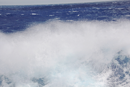 Storm waves in the world ocean. Kind of waves, crests, splashes, foam against the background of the sea horizon and the blue sky and clouds. A view of storm waves from the ship's side.の写真素材