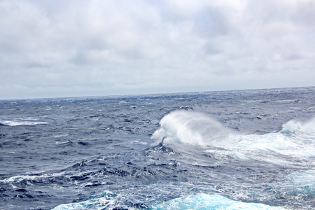 Storm waves in the world ocean. Kind of waves, crests, splashes, foam against the background of the sea horizon and the blue sky and clouds. A view of storm waves from the ship's side.の写真素材