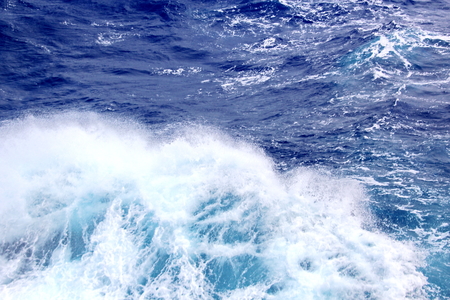 Storm waves in the world ocean. Kind of waves, crests, splashes, foam against the background of the sea horizon and the blue sky and clouds. A view of storm waves from the ship's side.の写真素材