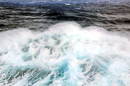 Storm waves in the world ocean. Kind of waves, crests, splashes, foam against the background of the sea horizon and the blue sky and clouds. A view of storm waves from the ship's side.の写真素材