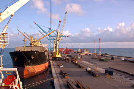 Transshipment terminal for loading steel products to sea vessels using shore cranes and special equipment. Vessels moored at berths and anchored in the roadstead. Sea and coastal line. Port Pecem, Brazil, June, 2017.の写真素材